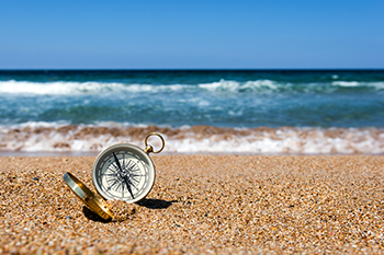 Gold compass on the beach sand ocean and blue sky representing directed trusts financial advisors